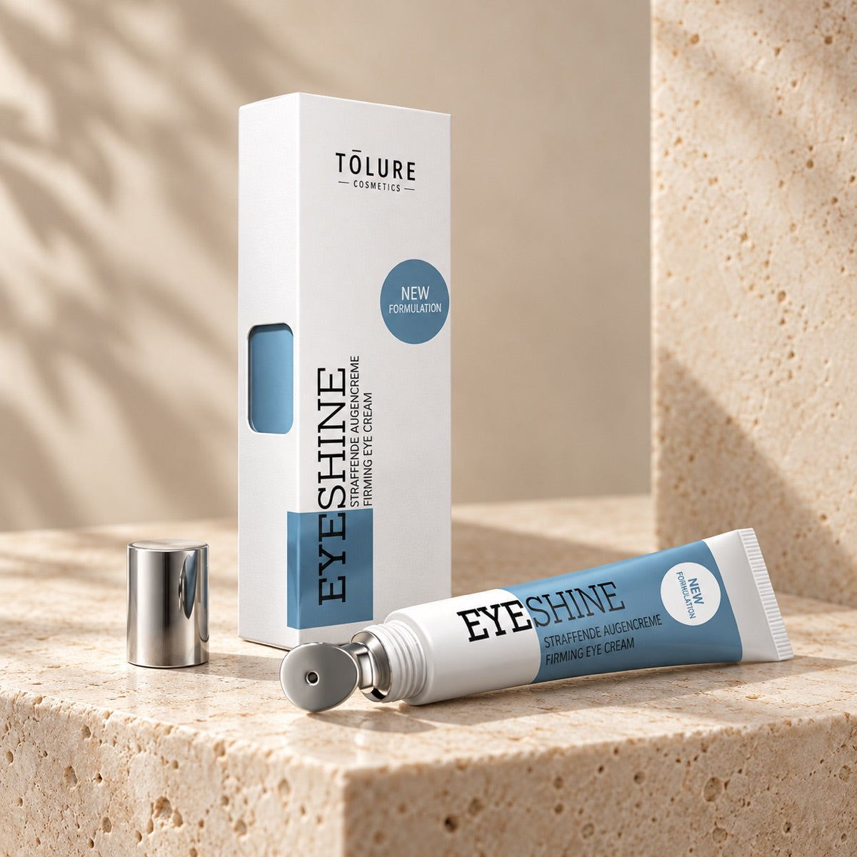 Detalje af et produkt i sættet: Tolure Eyeshine øjencreme 15 ml med metalapplikator, hætte og æske på travertin.
