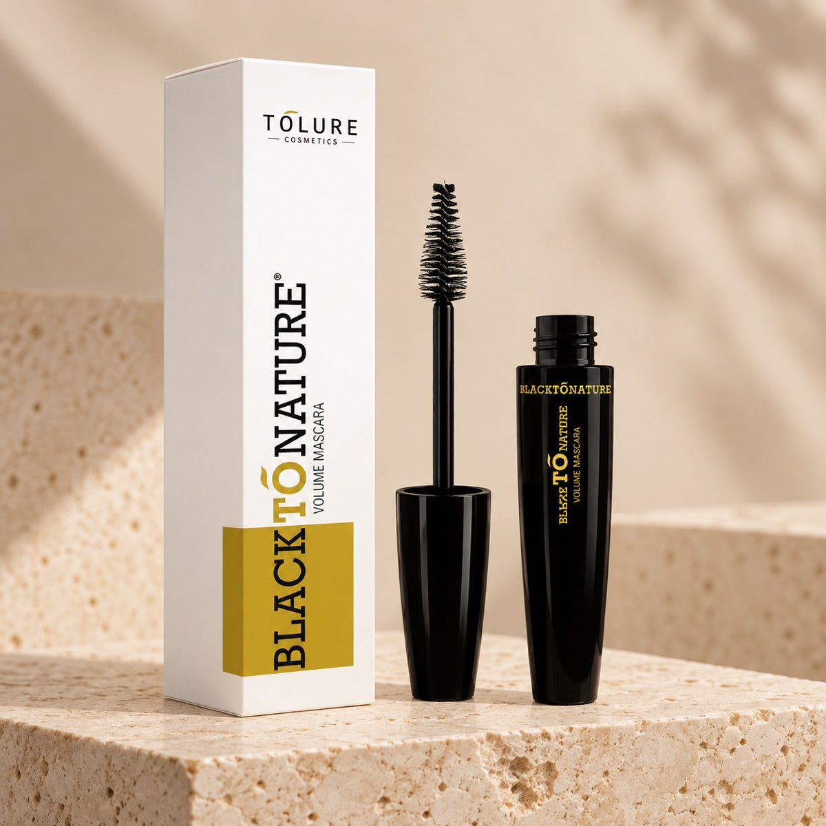 Detalje af et produkt i sættet: Tolure BlackToNature mascara 8,5 ml med børste og æske på lyst stenpodie.